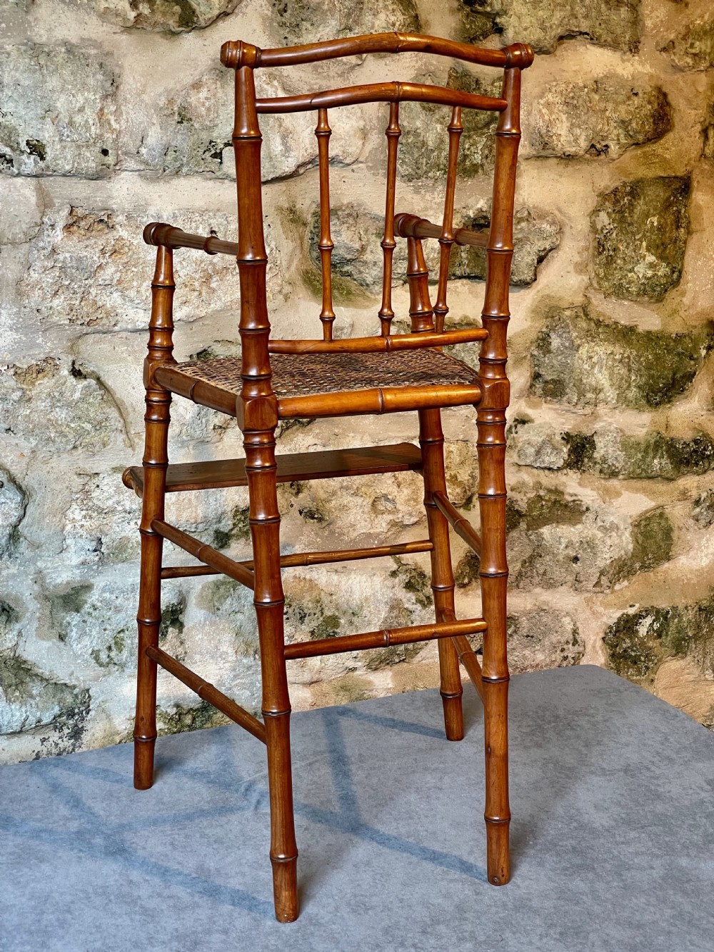 An antique Victorian faux bamboo turned wood childs high chair featuring a woven cane seat and integrated footrest. View XVII