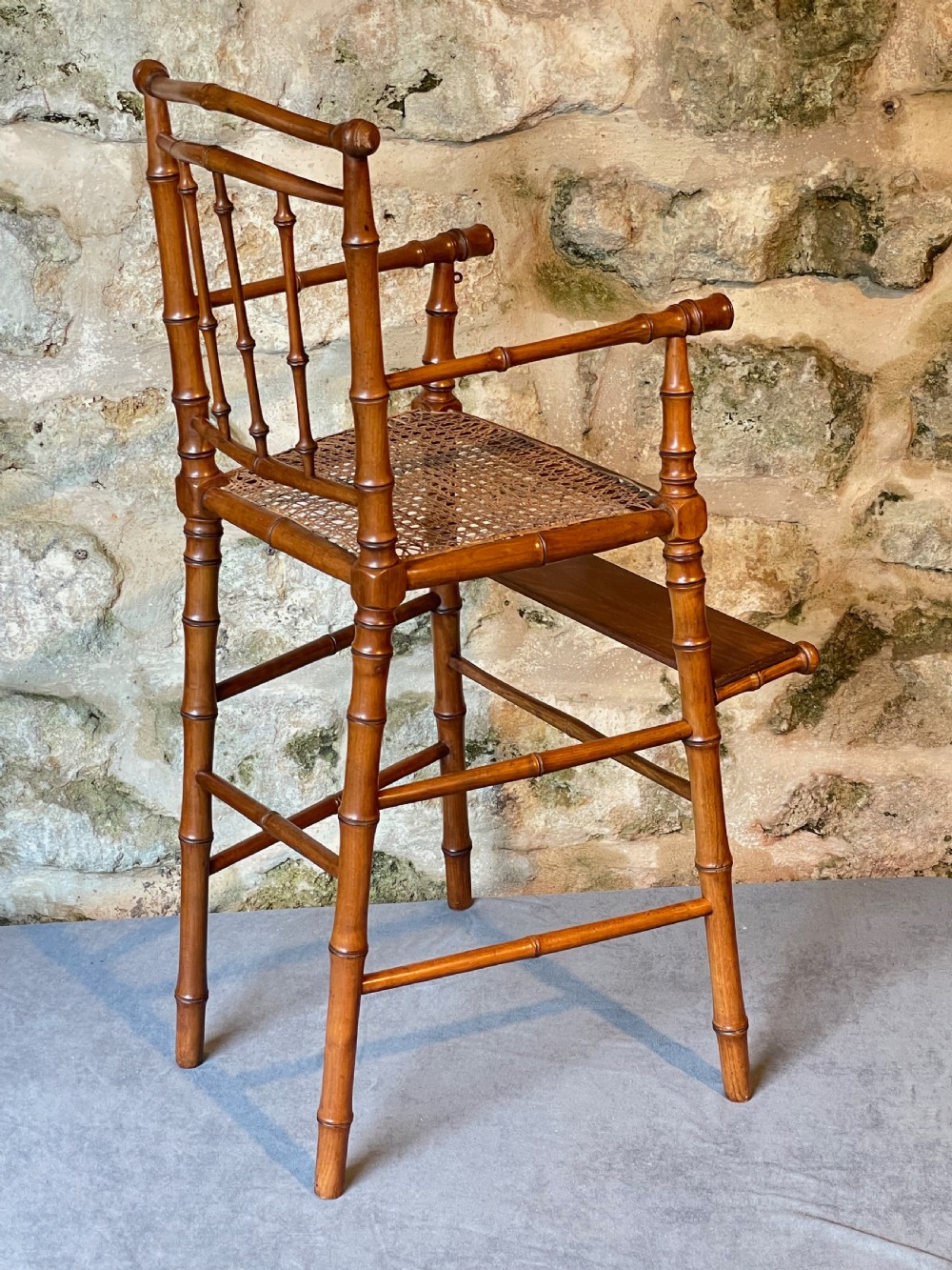 An antique Victorian faux bamboo turned wood childs high chair featuring a woven cane seat and integrated footrest. View XVIII