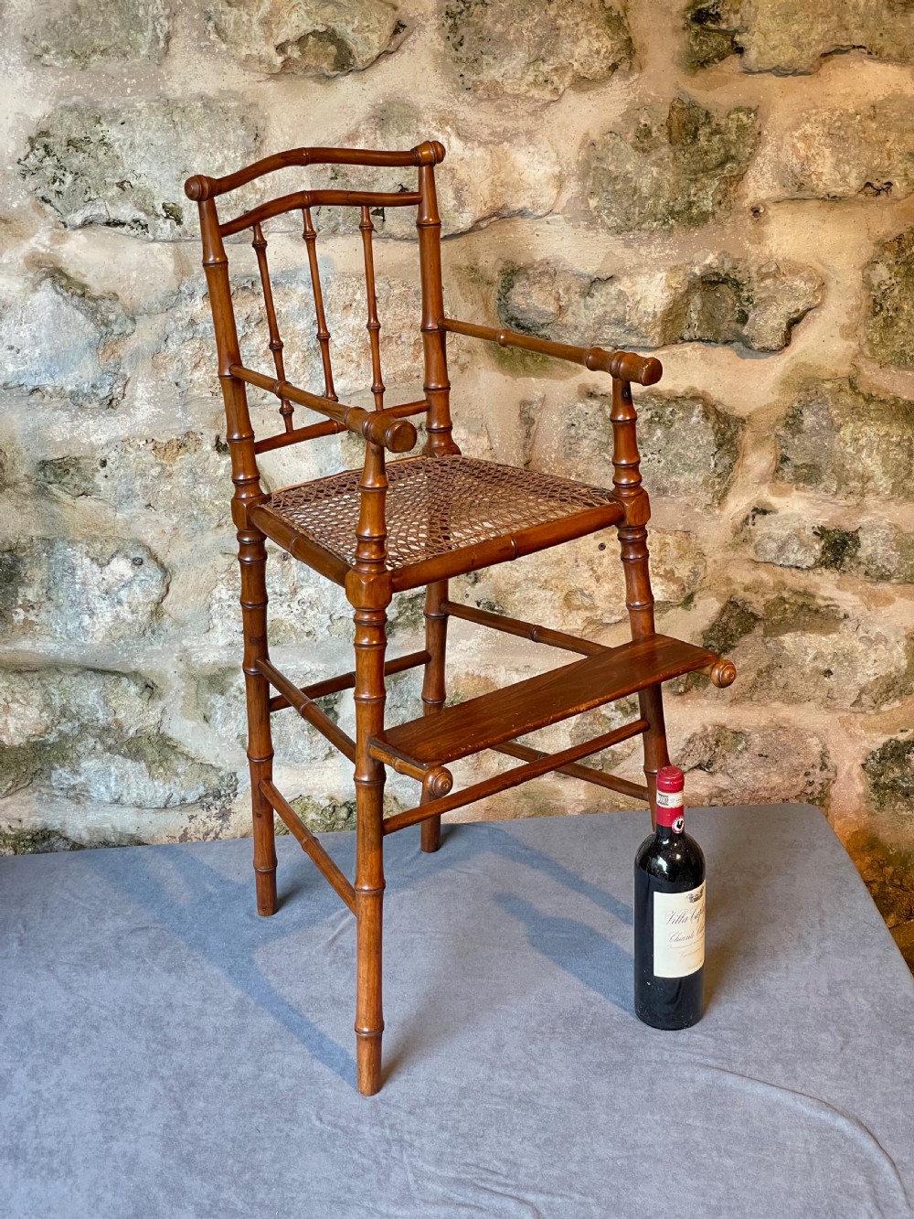 An antique Victorian faux bamboo turned wood childs high chair featuring a woven cane seat and integrated footrest. View XXI