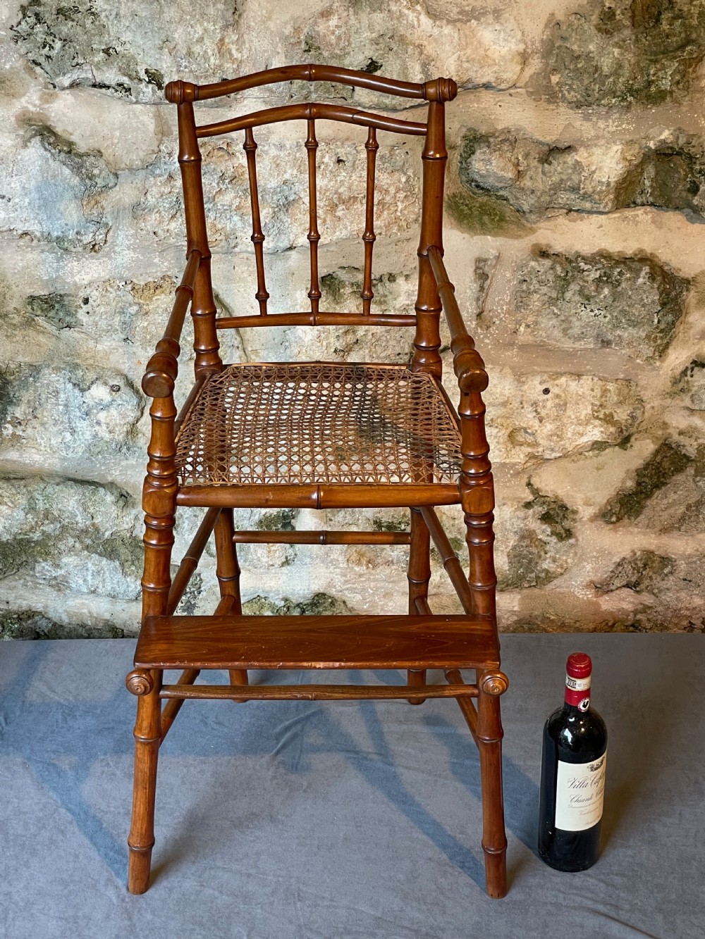 An antique Victorian faux bamboo turned wood childs high chair featuring a woven cane seat and integrated footrest. View XXIII