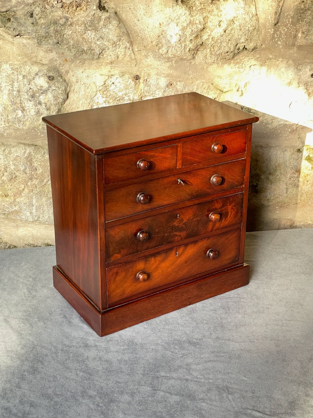 A miniature Victorian mahogany chest of drawers with two short over three long drawers, turned wooden knobs, and keyholes.