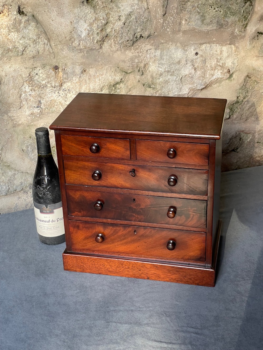 A miniature Victorian mahogany chest of drawers with two short over three long drawers, turned wooden knobs, and keyholes. View II