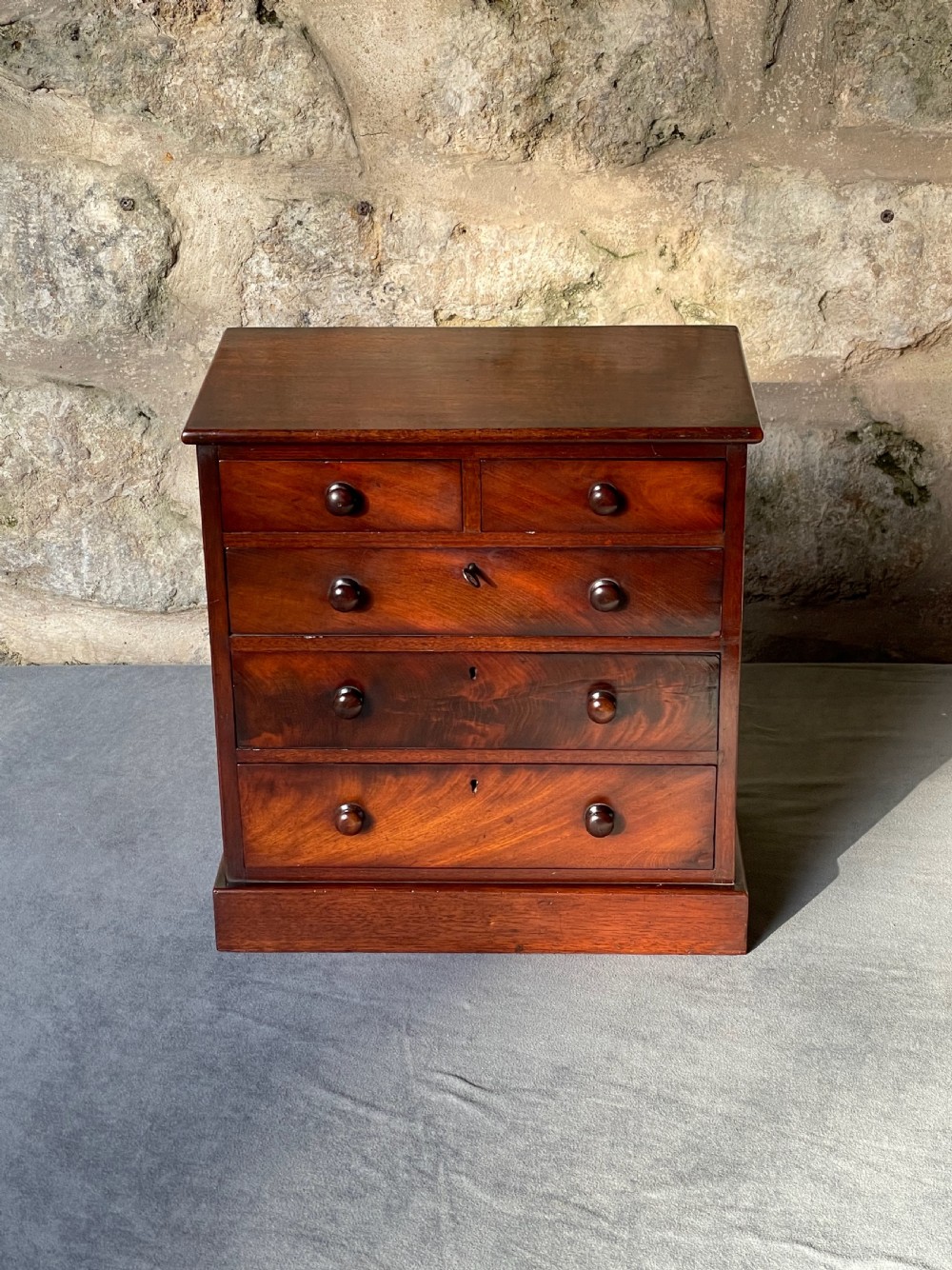 A miniature Victorian mahogany chest of drawers with two short over three long drawers, turned wooden knobs, and keyholes. View III