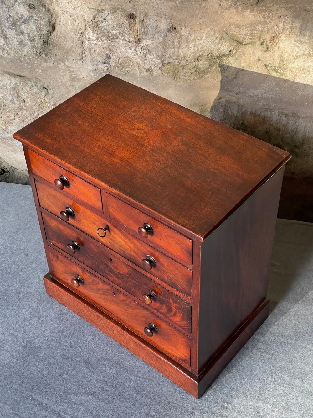 A miniature Victorian mahogany chest of drawers with two short over three long drawers, turned wooden knobs, and keyholes. View IV