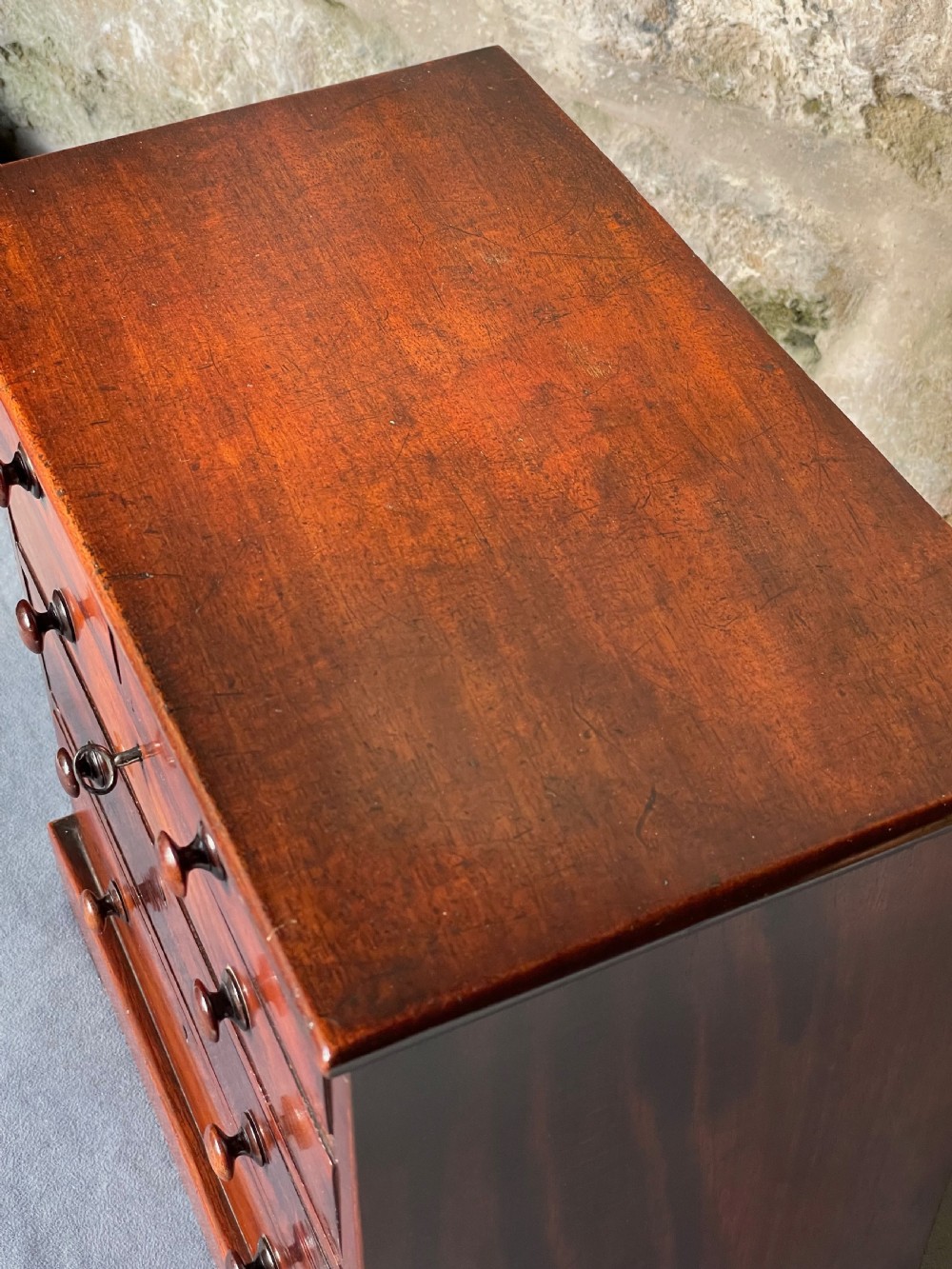 A miniature Victorian mahogany chest of drawers with two short over three long drawers, turned wooden knobs, and keyholes. View V