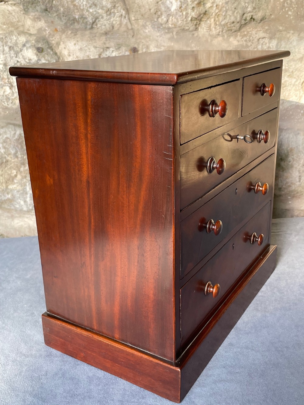 A miniature Victorian mahogany chest of drawers with two short over three long drawers, turned wooden knobs, and keyholes. View VII