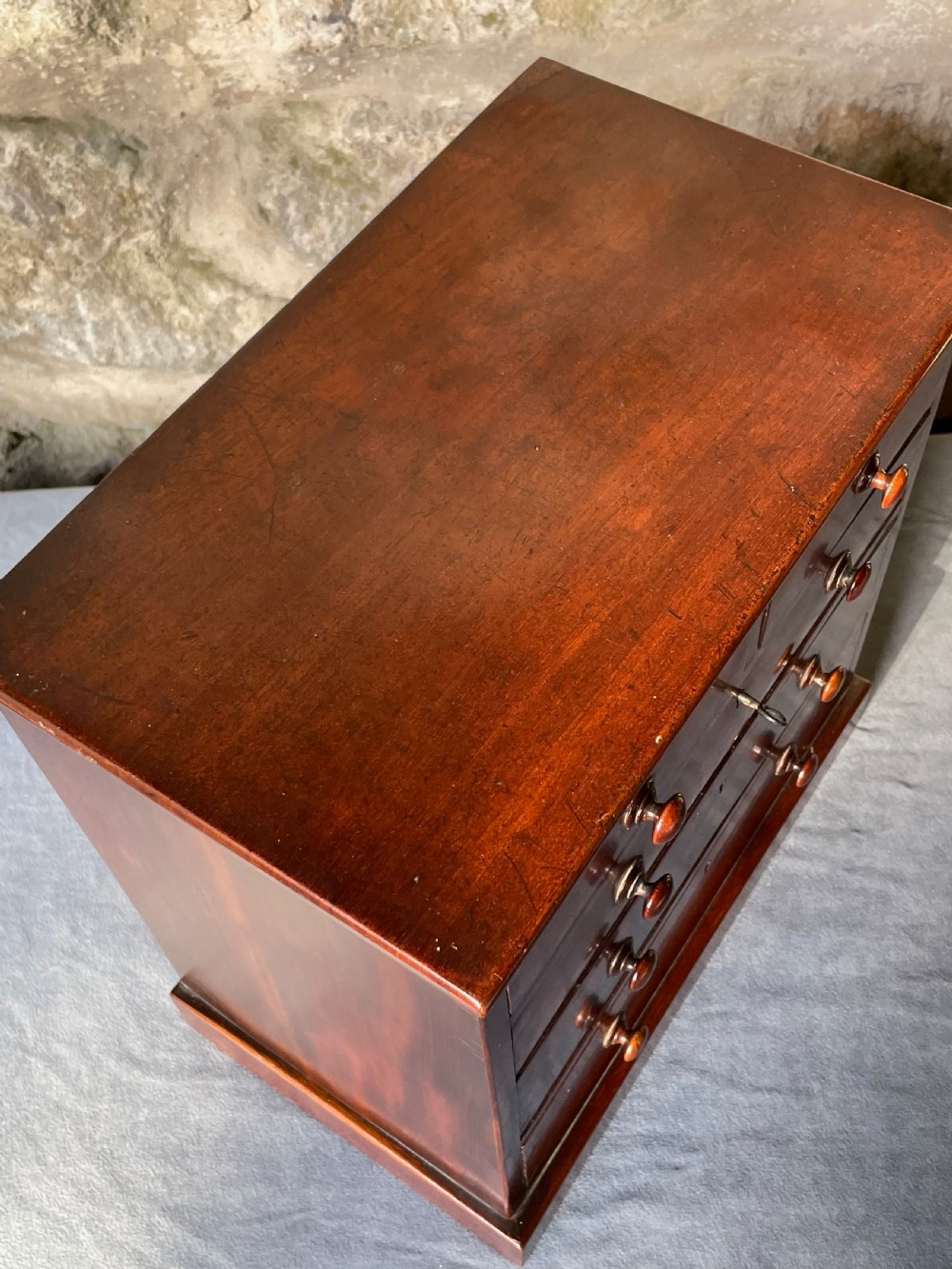 A miniature Victorian mahogany chest of drawers with two short over three long drawers, turned wooden knobs, and keyholes. View IX