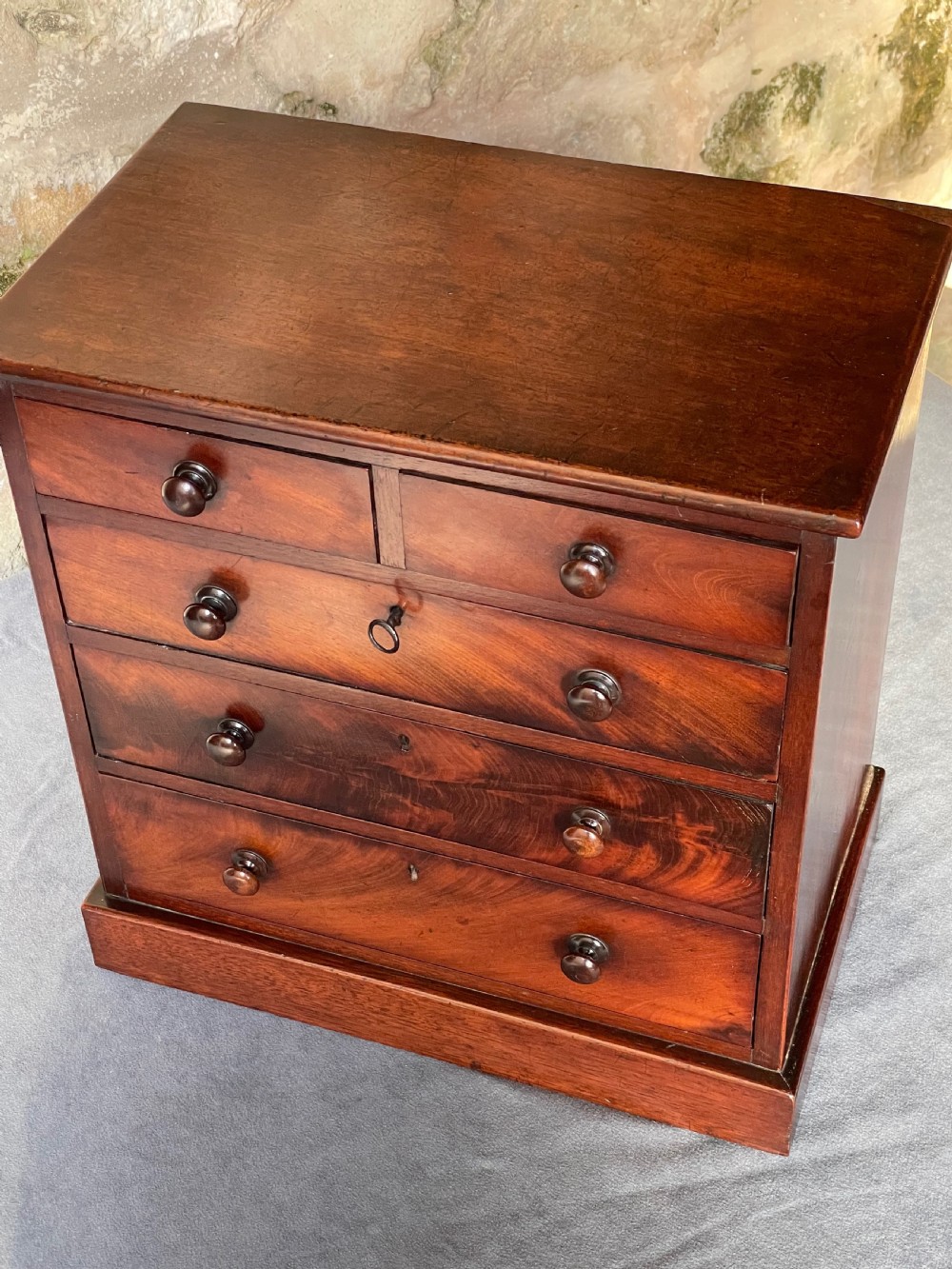 A miniature Victorian mahogany chest of drawers with two short over three long drawers, turned wooden knobs, and keyholes. View X
