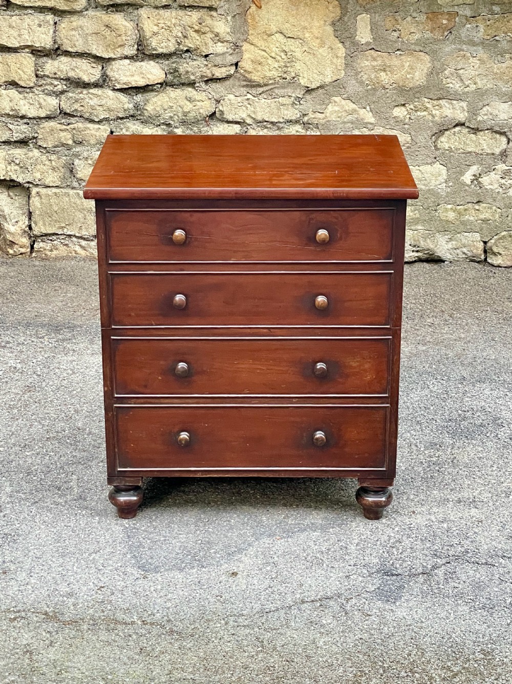 A Victorian warm brown wooden chest featuring four horizontal drawers with matching wooden knob handles and turned feet.
