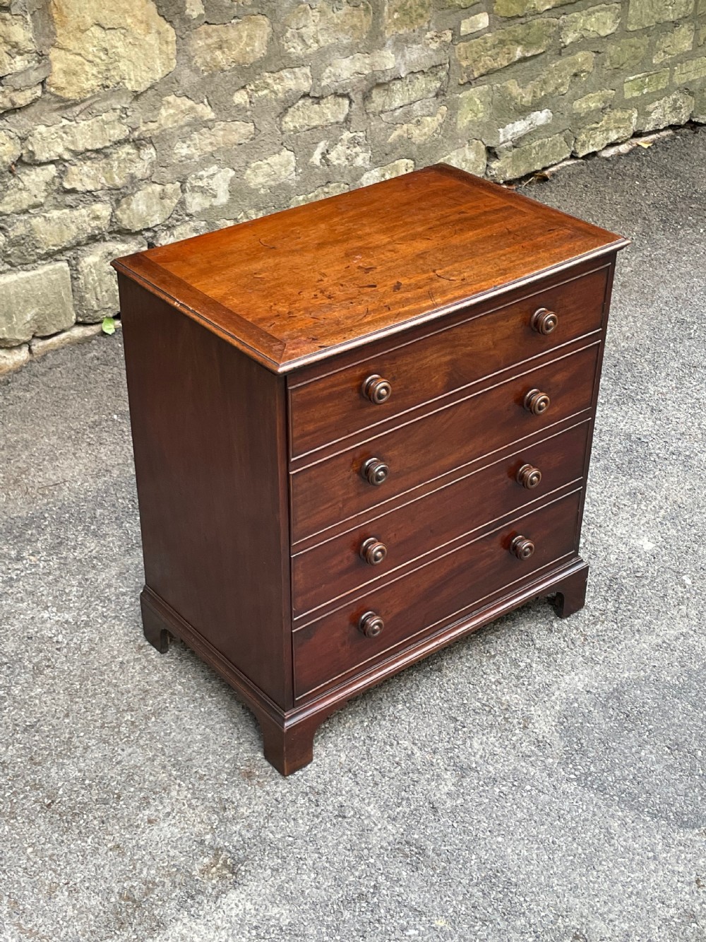 A Georgian mahogany chest featuring four drawer fronts with turned wooden handles and bracket feet. View IV