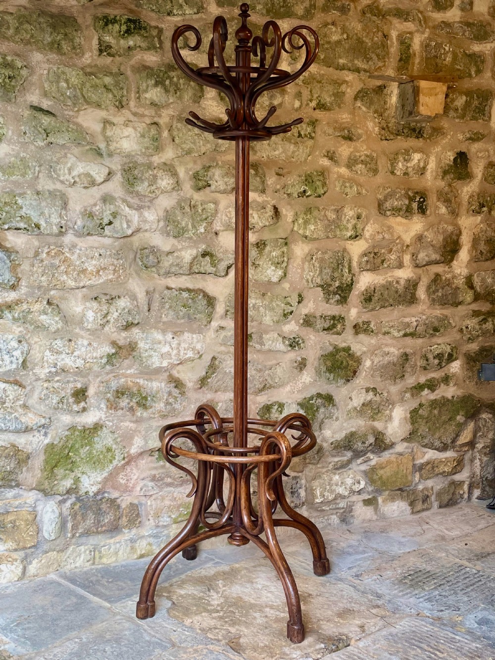 A dark brown bentwood hall stand featuring scrolled upper hooks for hats and coats, a central pole, and a curved lower frame for umbrellas.