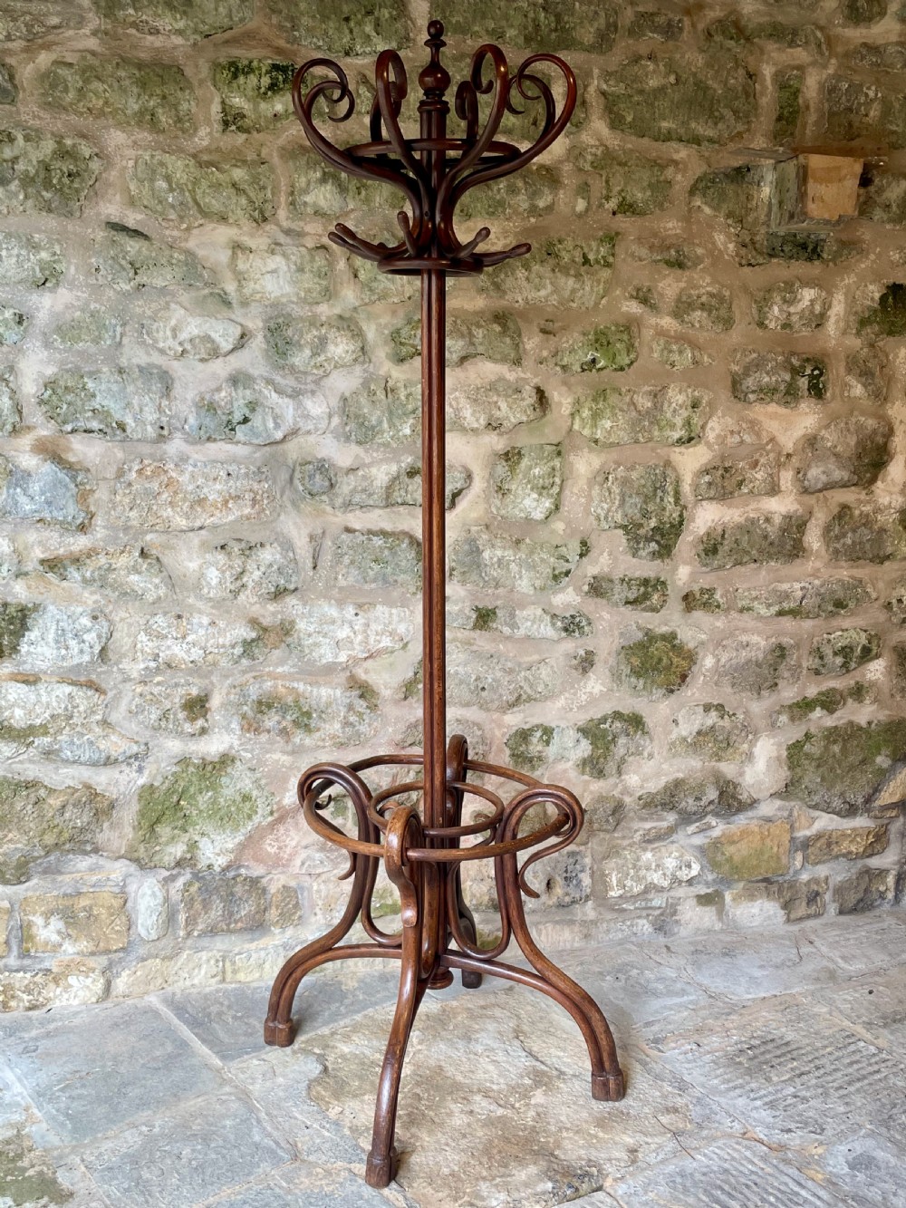 A dark brown bentwood hall stand featuring scrolled upper hooks for hats and coats, a central pole, and a curved lower frame for umbrellas. View II