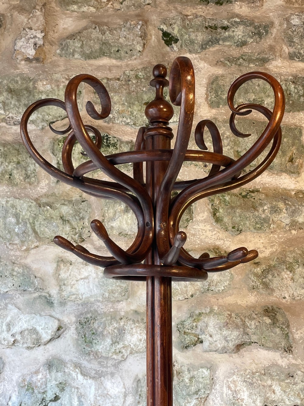 A dark brown bentwood hall stand featuring scrolled upper hooks for hats and coats, a central pole, and a curved lower frame for umbrellas. View V