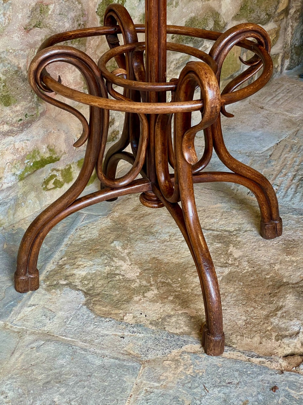 A dark brown bentwood hall stand featuring scrolled upper hooks for hats and coats, a central pole, and a curved lower frame for umbrellas. View X