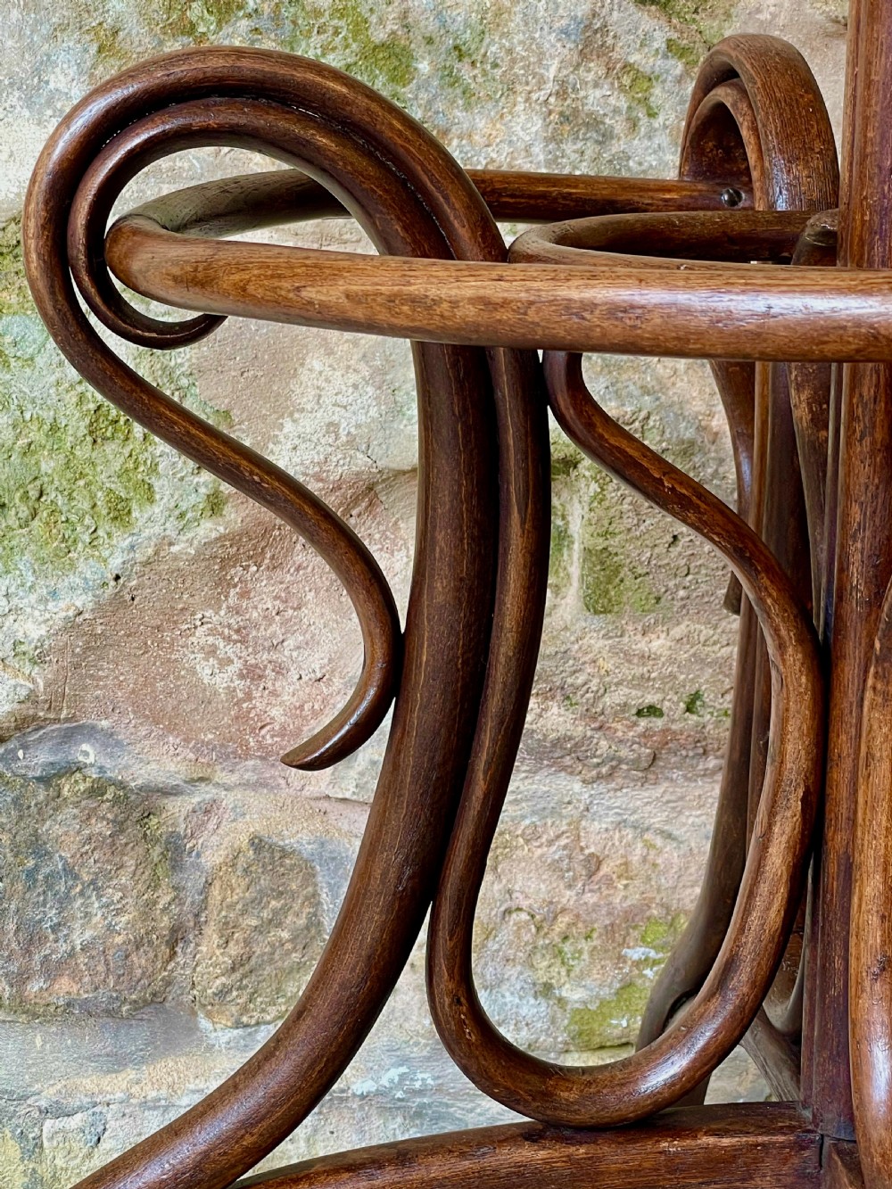 A dark brown bentwood hall stand featuring scrolled upper hooks for hats and coats, a central pole, and a curved lower frame for umbrellas. View XII