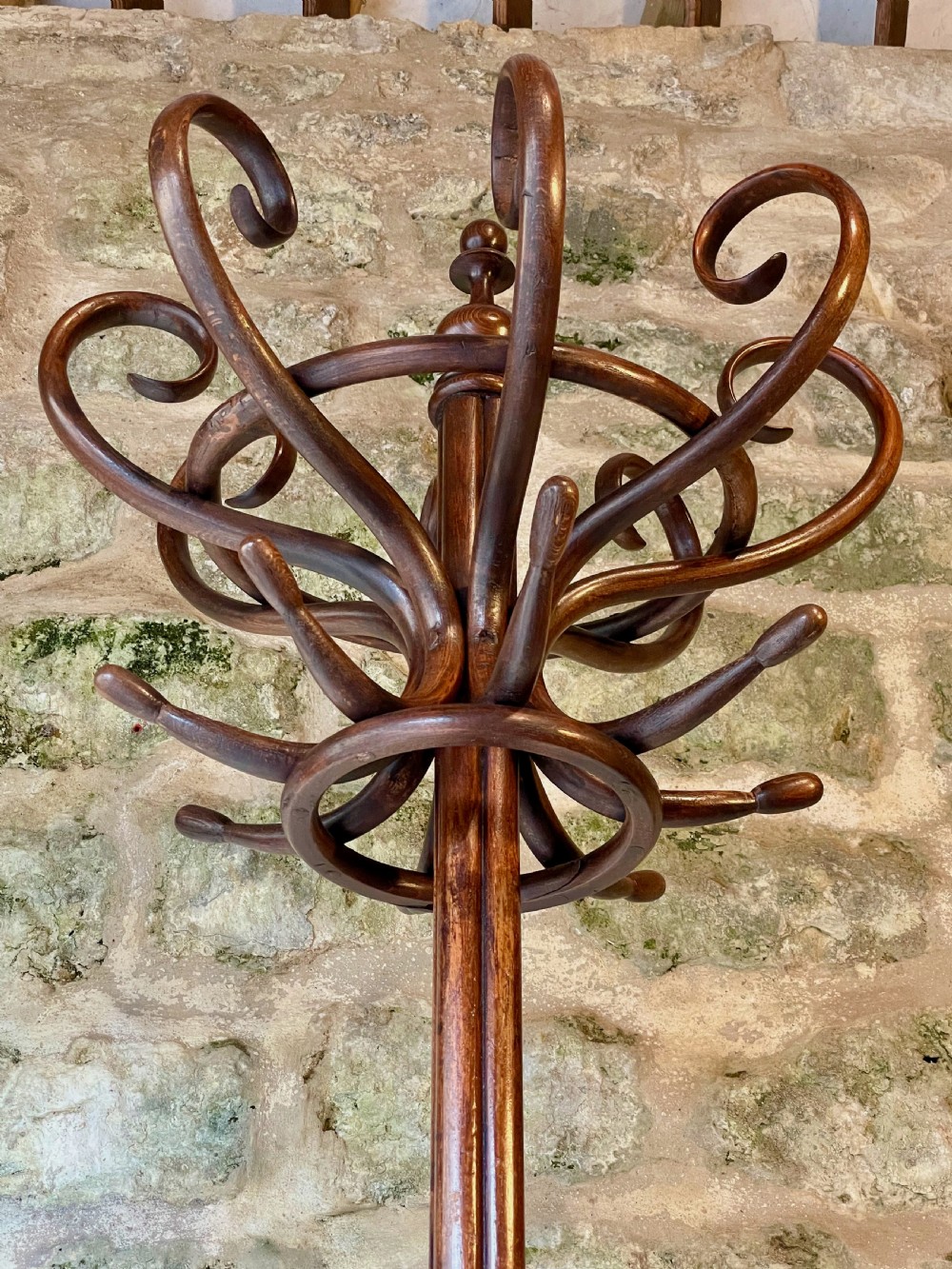 A dark brown bentwood hall stand featuring scrolled upper hooks for hats and coats, a central pole, and a curved lower frame for umbrellas. View XIII