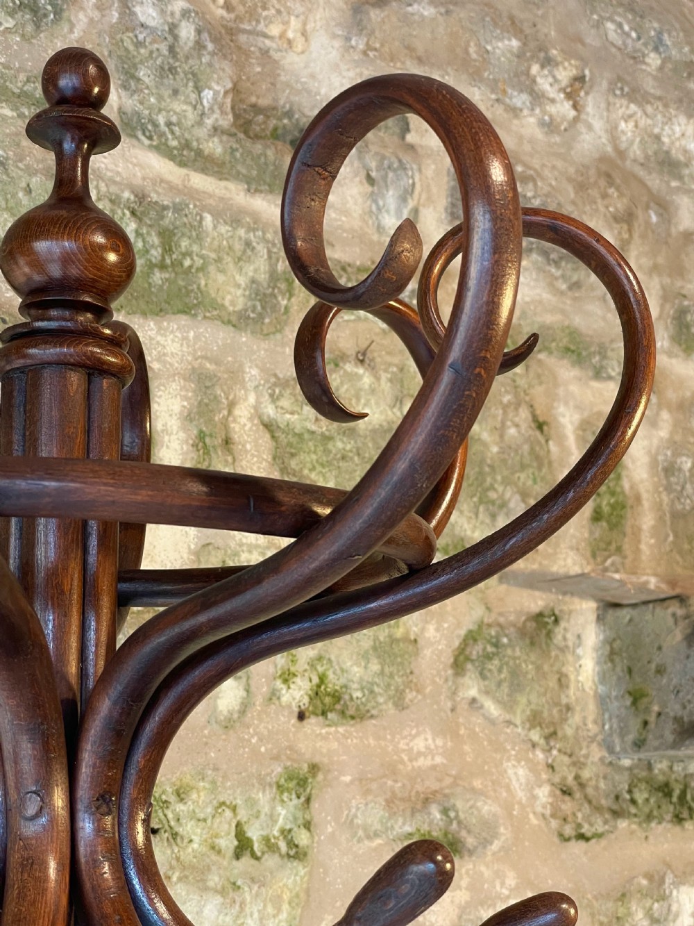 A dark brown bentwood hall stand featuring scrolled upper hooks for hats and coats, a central pole, and a curved lower frame for umbrellas. View XVI