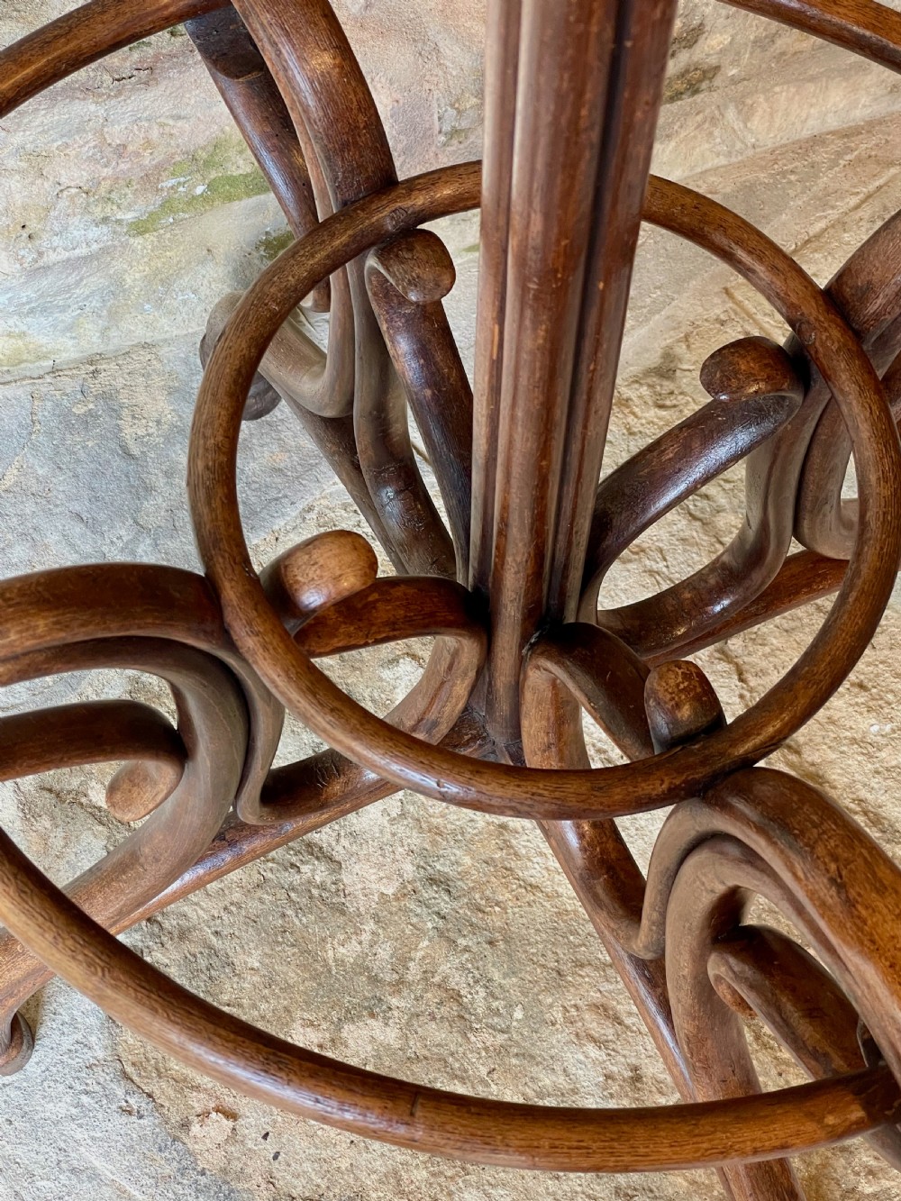 A dark brown bentwood hall stand featuring scrolled upper hooks for hats and coats, a central pole, and a curved lower frame for umbrellas. View XVII