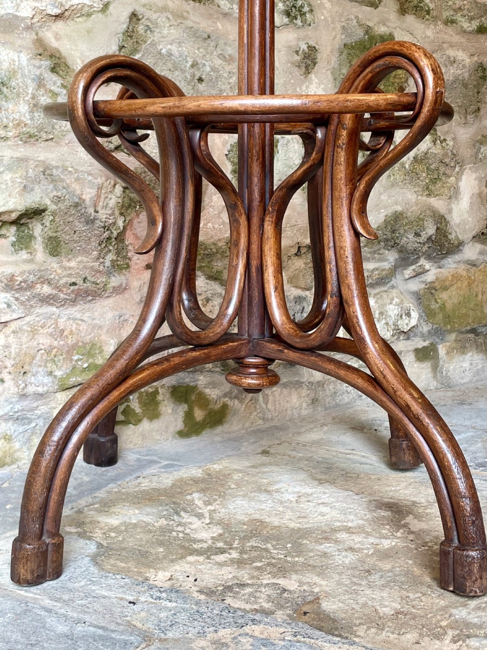 A dark brown bentwood hall stand featuring scrolled upper hooks for hats and coats, a central pole, and a curved lower frame for umbrellas. View XIX