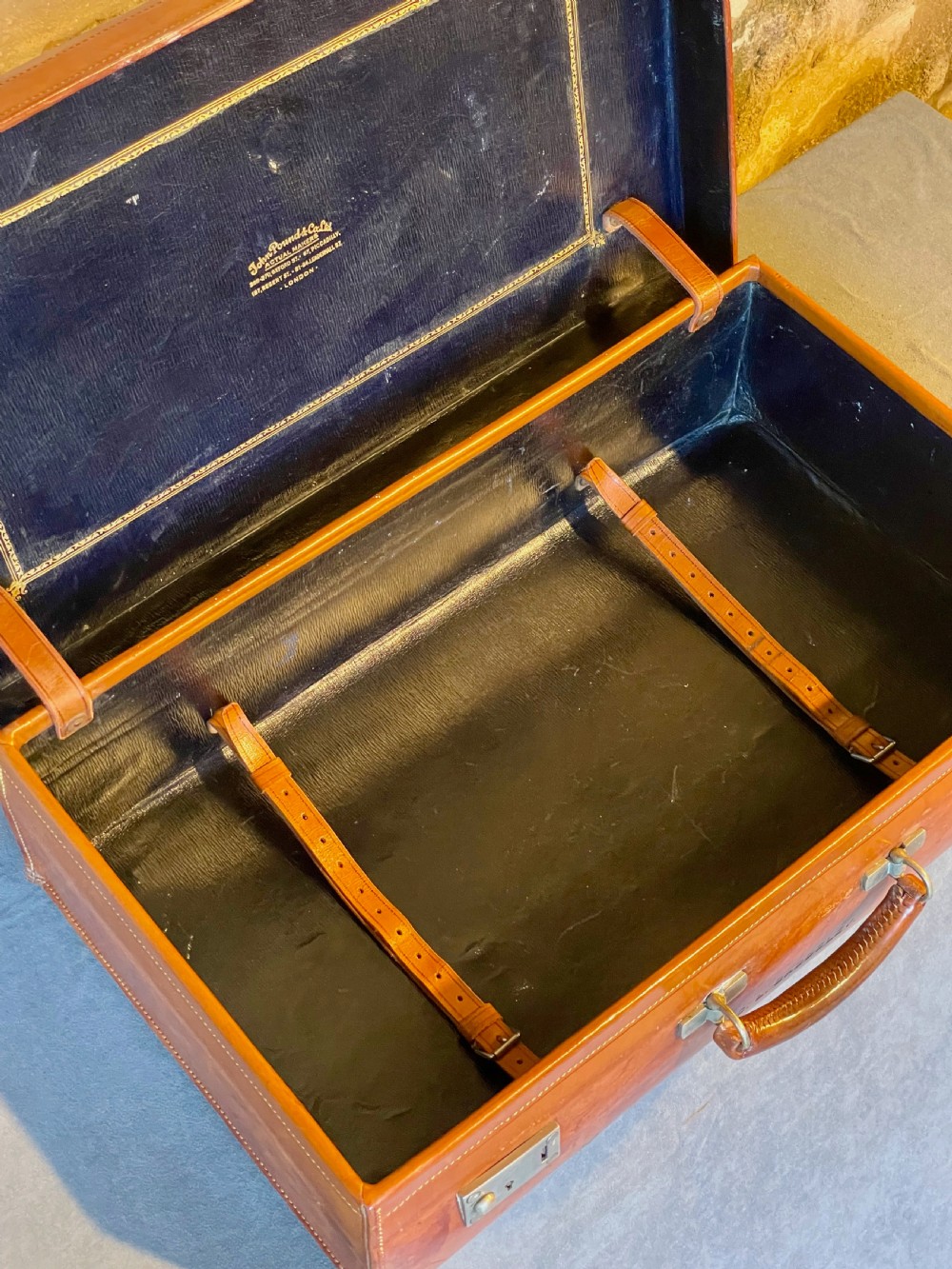 A rectangular chestnut brown leather suitcase featuring twin metal latches, hand-stitched edges, and a central leather carrying handle. View XIV
