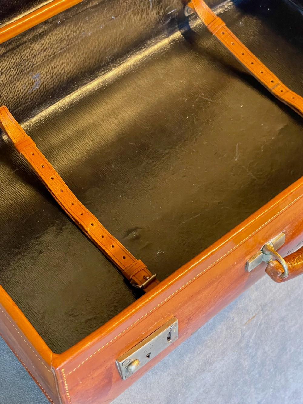 A rectangular chestnut brown leather suitcase featuring twin metal latches, hand-stitched edges, and a central leather carrying handle. View XV