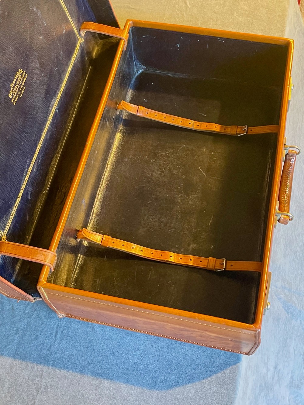 A rectangular chestnut brown leather suitcase featuring twin metal latches, hand-stitched edges, and a central leather carrying handle. View XVIII