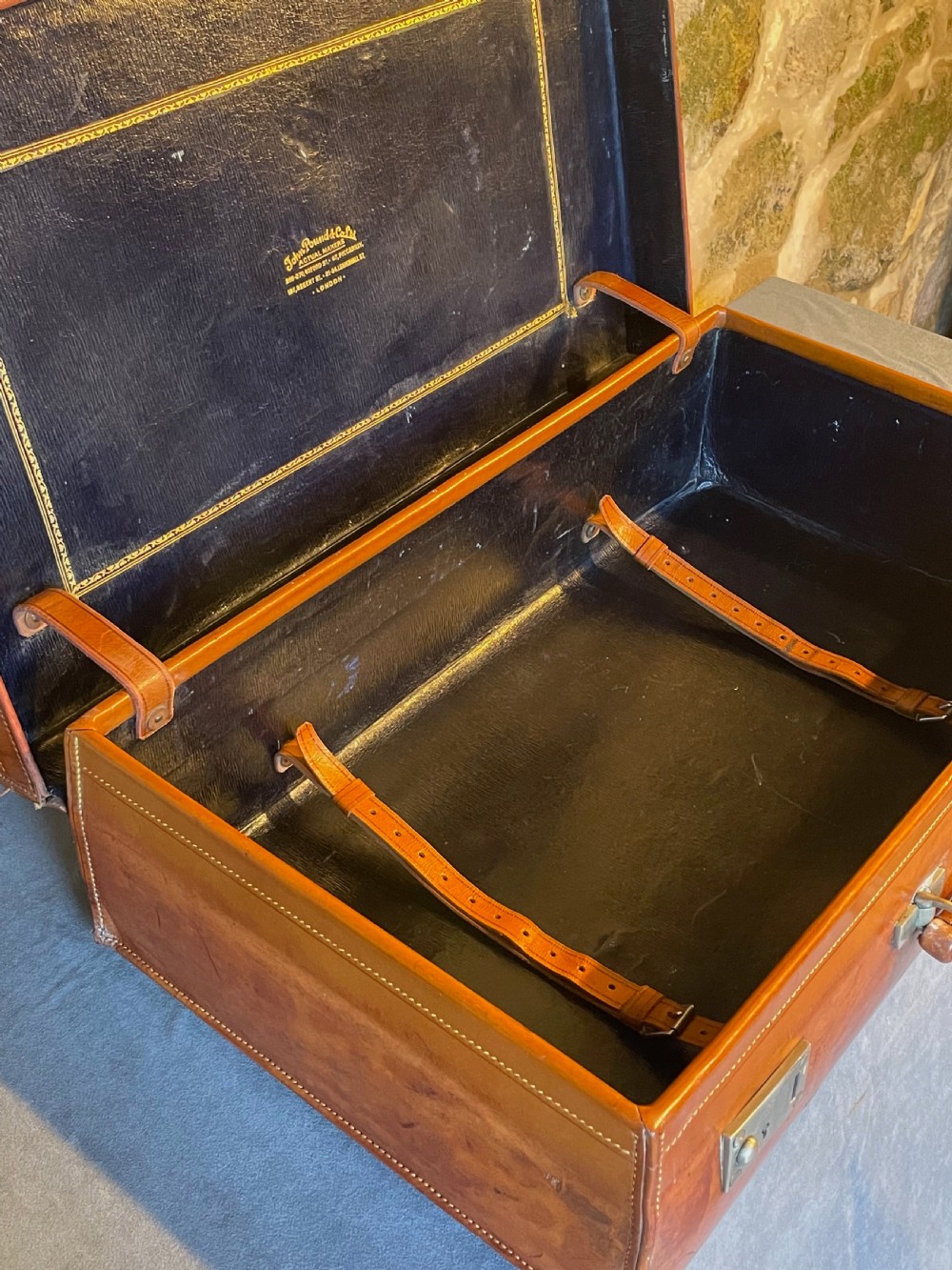 A rectangular chestnut brown leather suitcase featuring twin metal latches, hand-stitched edges, and a central leather carrying handle. View XIX