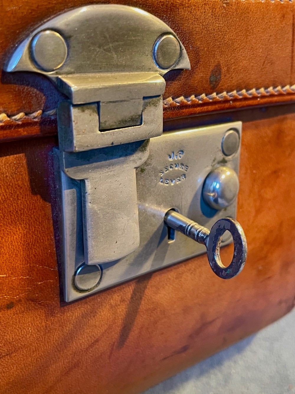 A rectangular chestnut brown leather suitcase featuring twin metal latches, hand-stitched edges, and a central leather carrying handle. View XX