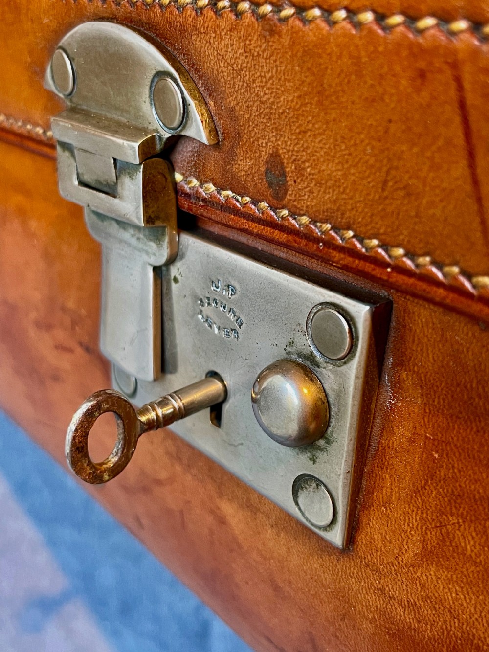 A rectangular chestnut brown leather suitcase featuring twin metal latches, hand-stitched edges, and a central leather carrying handle. View XXI