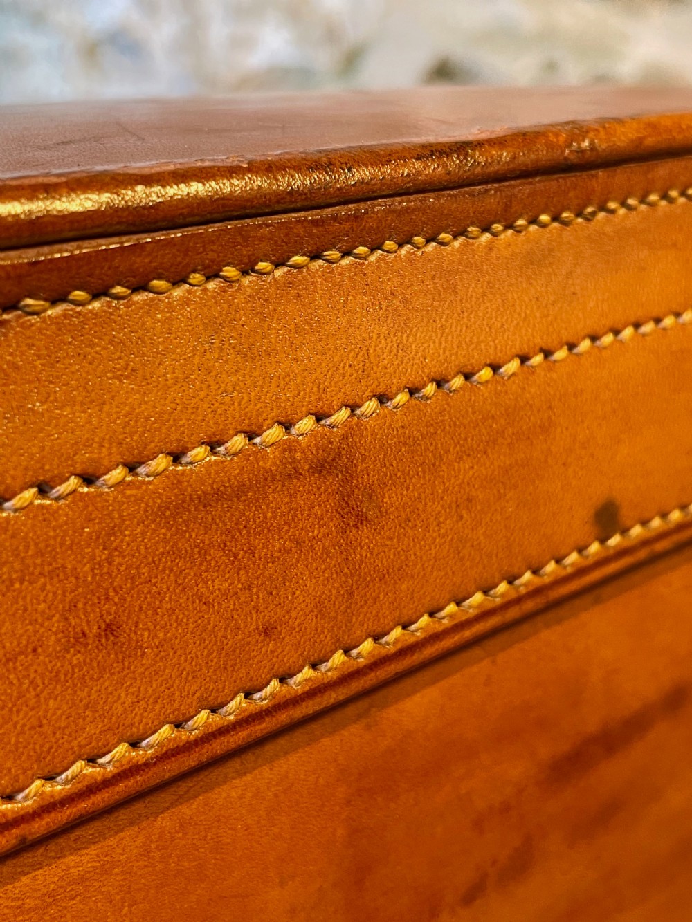 A rectangular chestnut brown leather suitcase featuring twin metal latches, hand-stitched edges, and a central leather carrying handle. View XXIV
