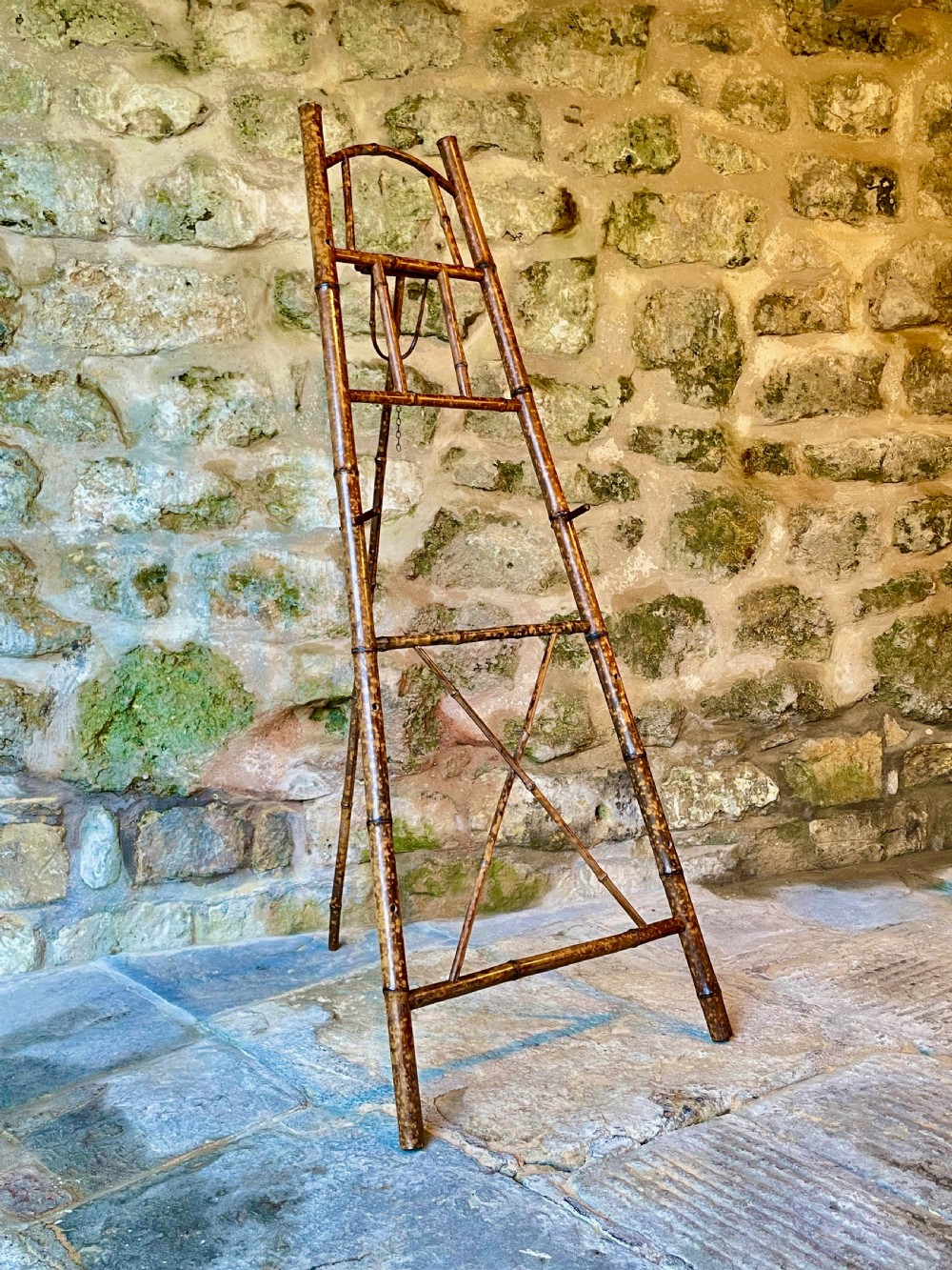 A tall Victorian freestanding easel crafted from mottled brown bamboo with cross-bracing and support pegs.