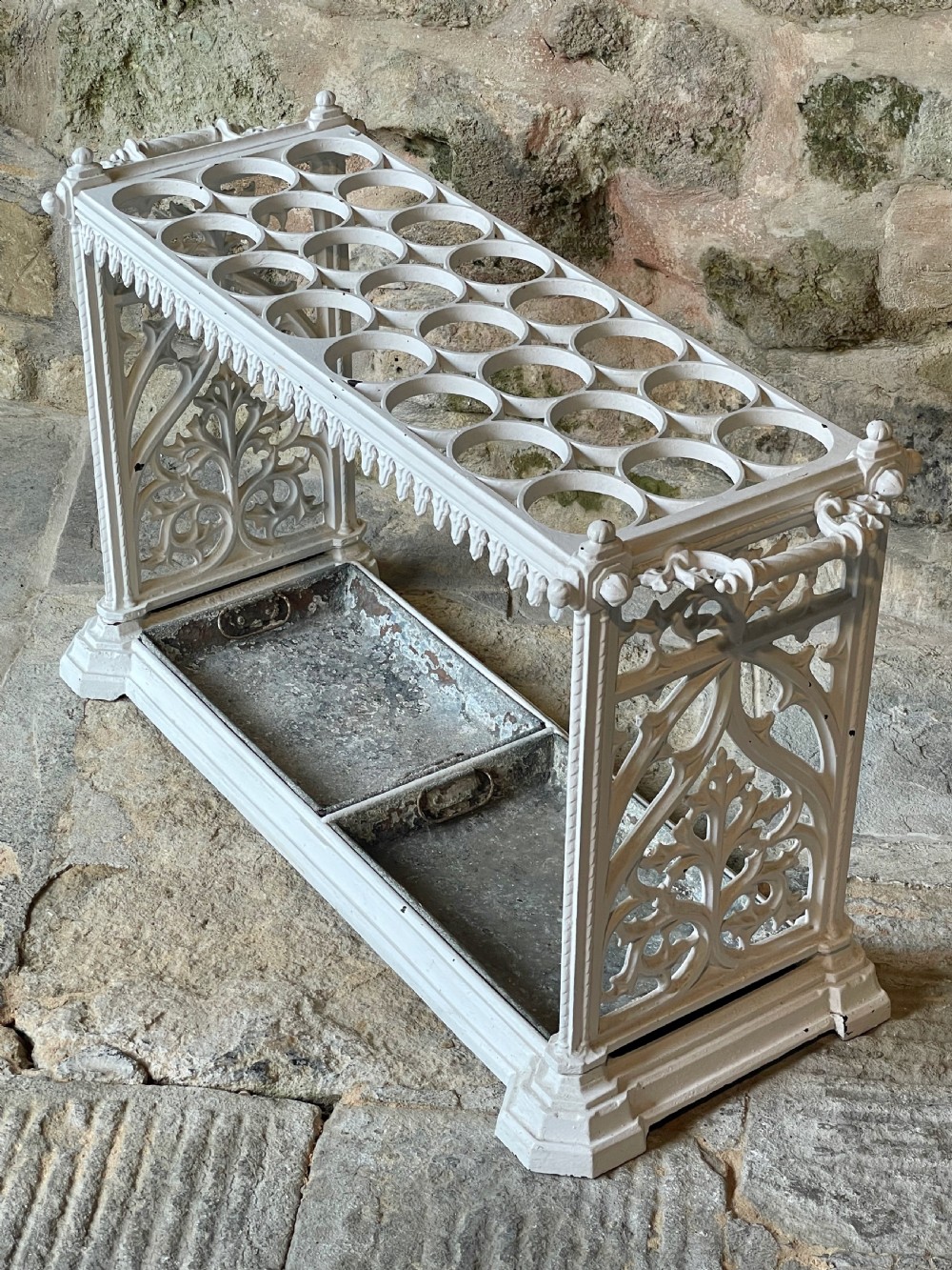 A white painted cast iron stick stand featuring openwork Gothic tracery side panels, a circular grid top section, and a removable double drip tray.