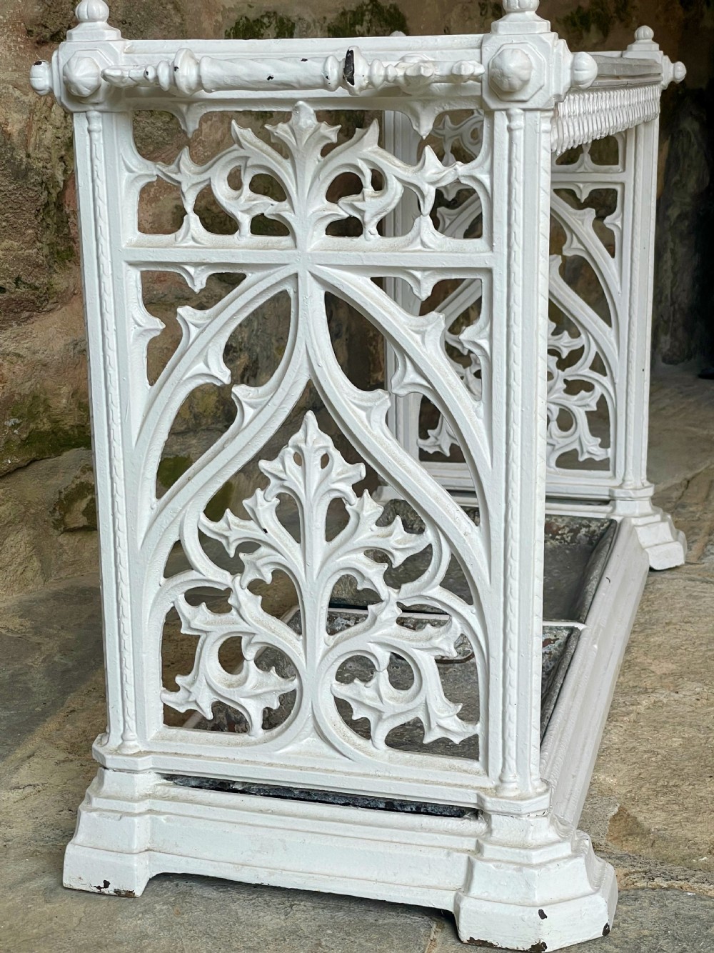 A white painted cast iron stick stand featuring openwork Gothic tracery side panels, a circular grid top section, and a removable double drip tray. View IX
