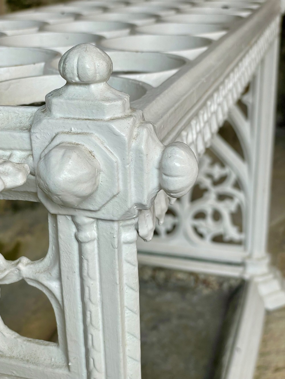 A white painted cast iron stick stand featuring openwork Gothic tracery side panels, a circular grid top section, and a removable double drip tray. View XI