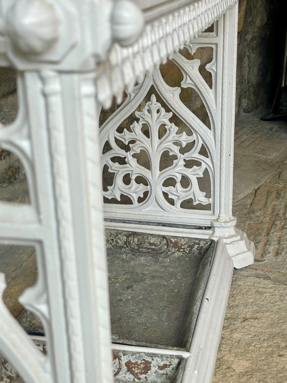 A white painted cast iron stick stand featuring openwork Gothic tracery side panels, a circular grid top section, and a removable double drip tray. View XII