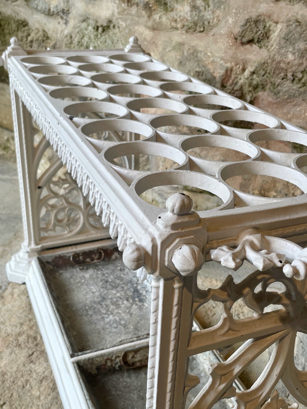 A white painted cast iron stick stand featuring openwork Gothic tracery side panels, a circular grid top section, and a removable double drip tray. View XIX