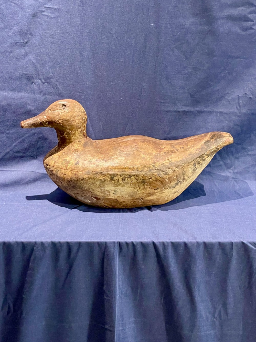 A hand-carved wooden decoy duck featuring a rounded body, defined head, and visible wood grain patination across the natural timber surface.