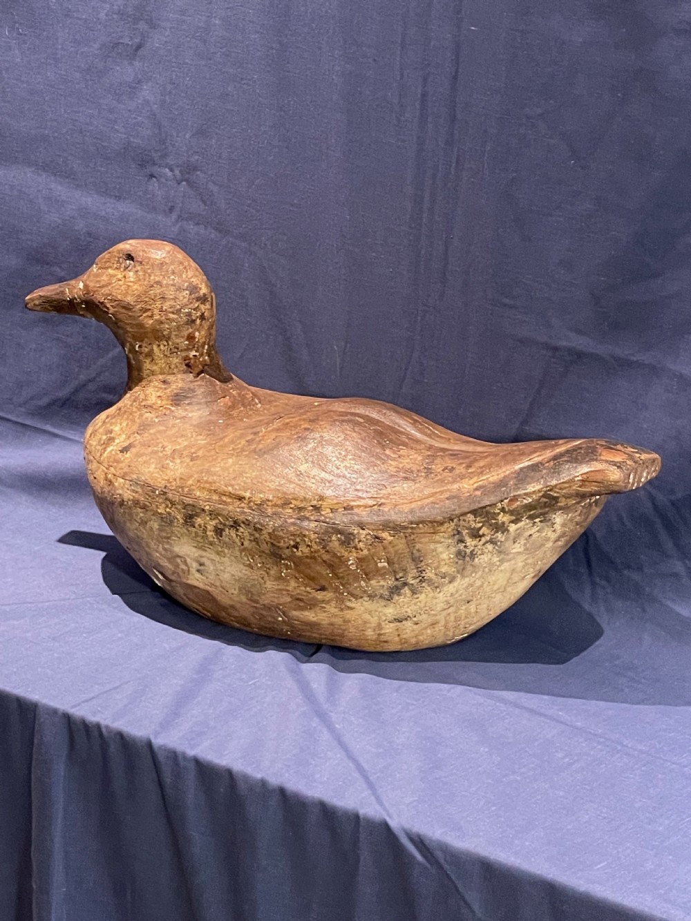 A hand-carved wooden decoy duck featuring a rounded body, defined head, and visible wood grain patination across the natural timber surface. View III