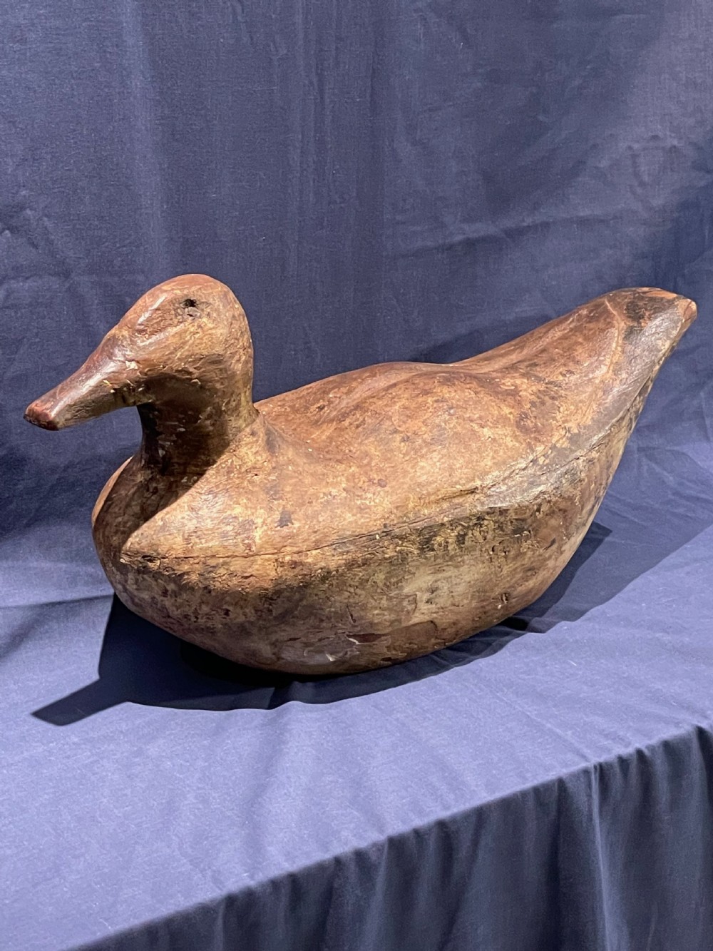 A hand-carved wooden decoy duck featuring a rounded body, defined head, and visible wood grain patination across the natural timber surface. View V