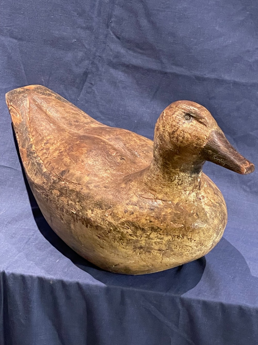 A hand-carved wooden decoy duck featuring a rounded body, defined head, and visible wood grain patination across the natural timber surface. View VI