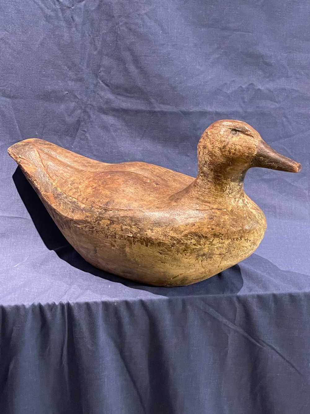 A hand-carved wooden decoy duck featuring a rounded body, defined head, and visible wood grain patination across the natural timber surface. View VII