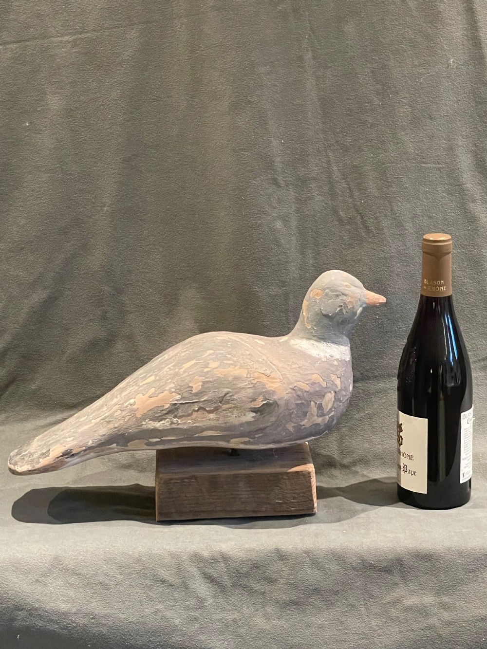 A hand-carved wooden pigeon decoy featuring weathered grey paint, mounted on a small rectangular wooden block. View II