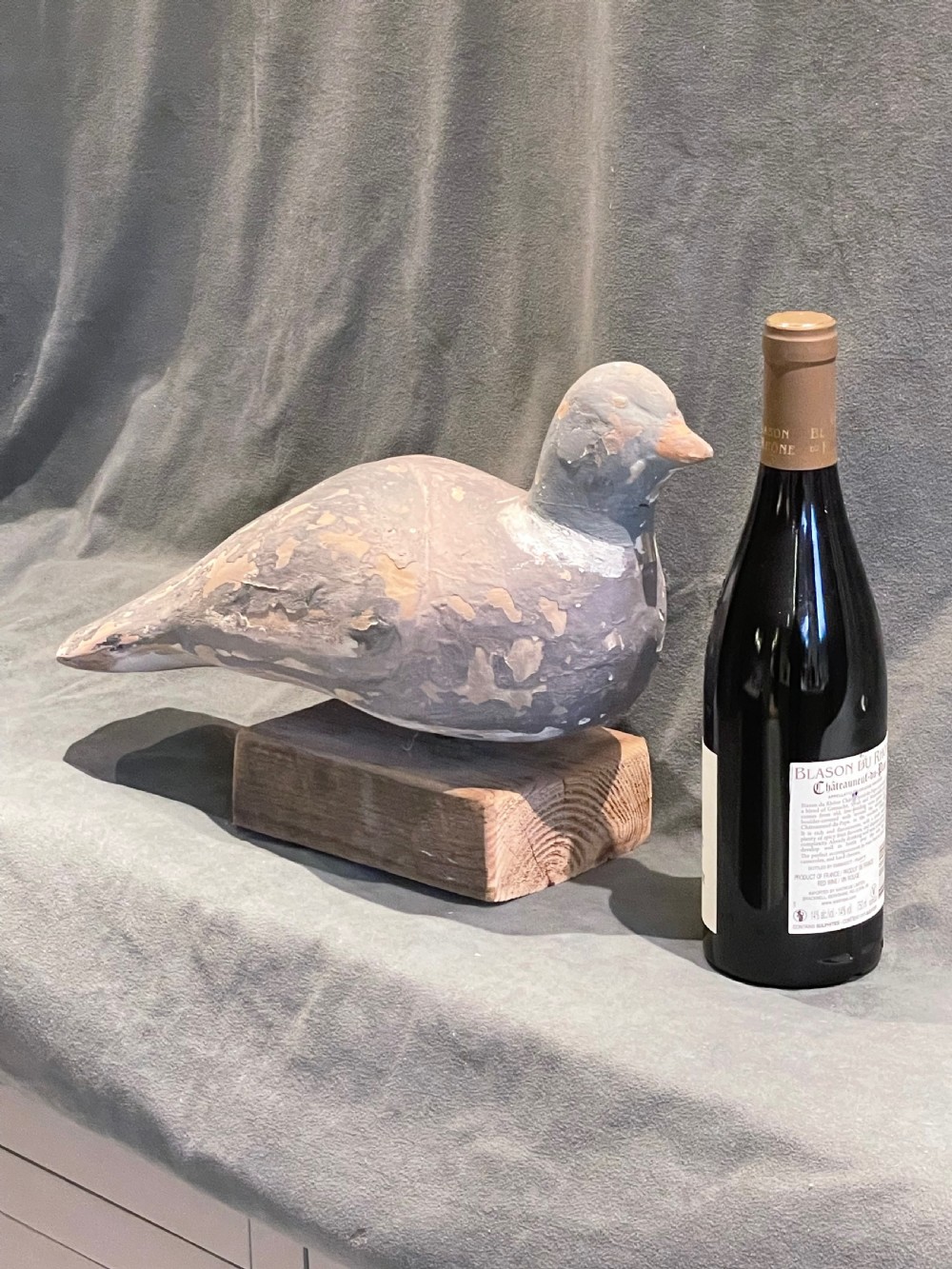 A hand-carved wooden pigeon decoy featuring weathered grey paint, mounted on a small rectangular wooden block. View III