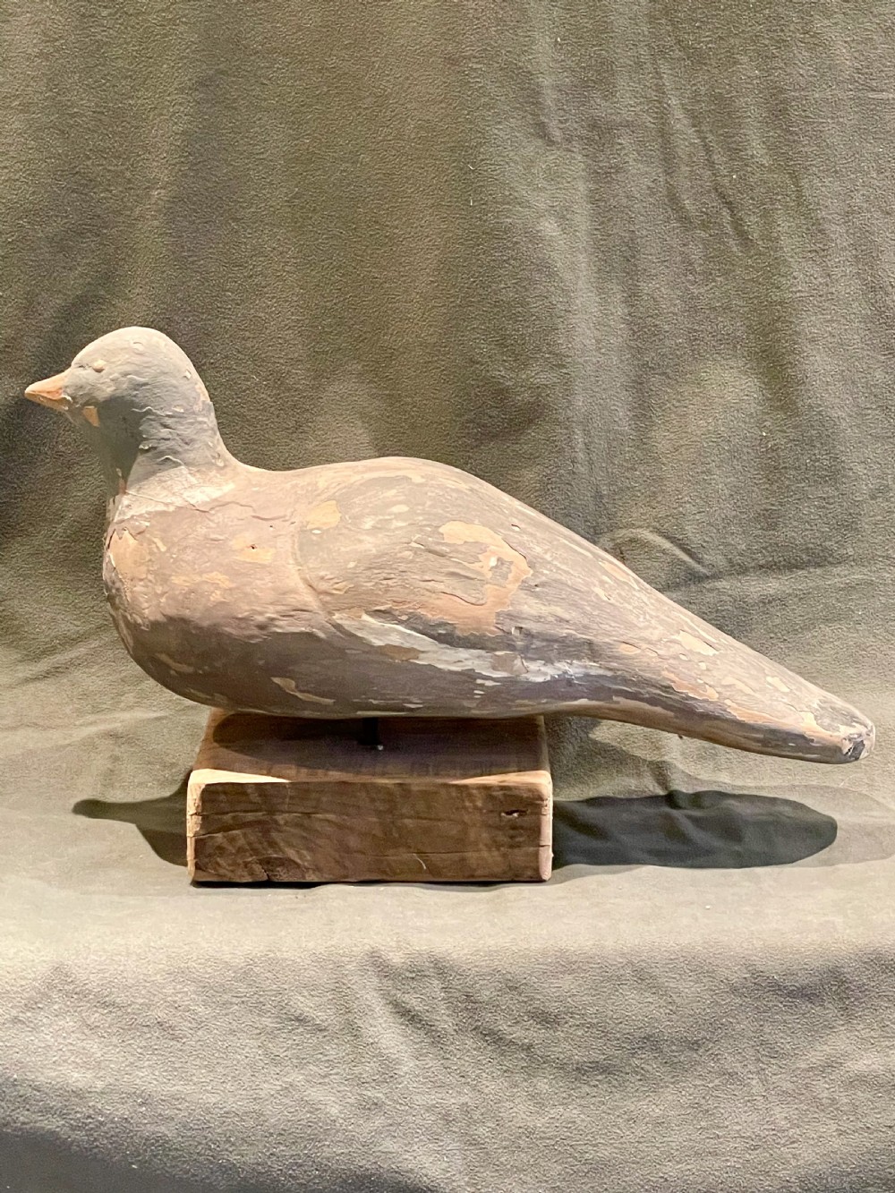 A hand-carved wooden pigeon decoy featuring weathered grey paint, mounted on a small rectangular wooden block. View V