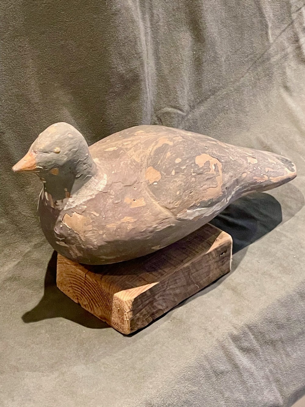 A hand-carved wooden pigeon decoy featuring weathered grey paint, mounted on a small rectangular wooden block. View VII