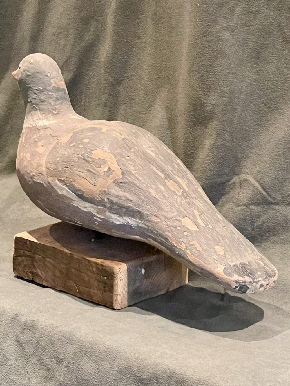 A hand-carved wooden pigeon decoy featuring weathered grey paint, mounted on a small rectangular wooden block. View VIII