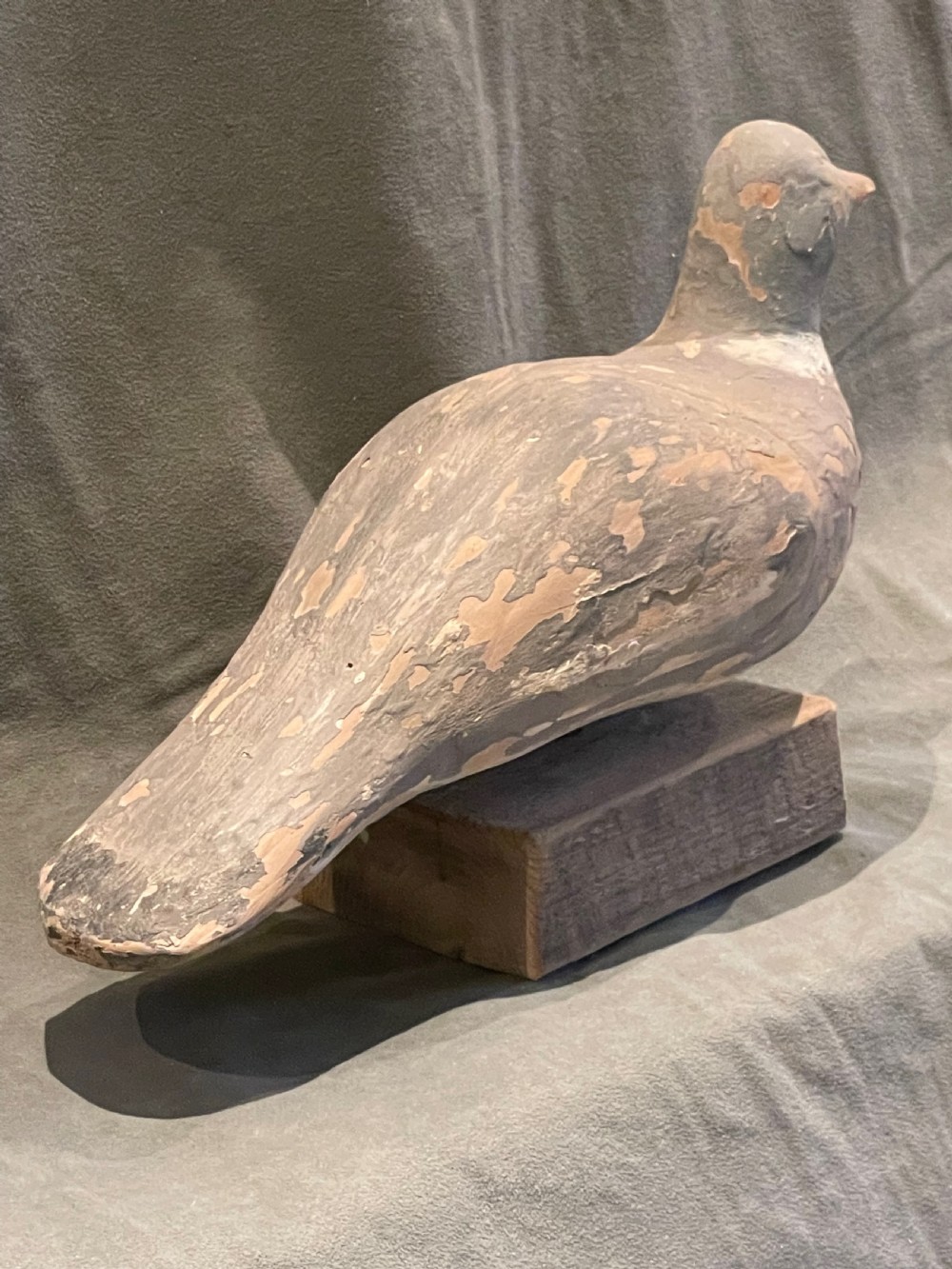 A hand-carved wooden pigeon decoy featuring weathered grey paint, mounted on a small rectangular wooden block. View XIV