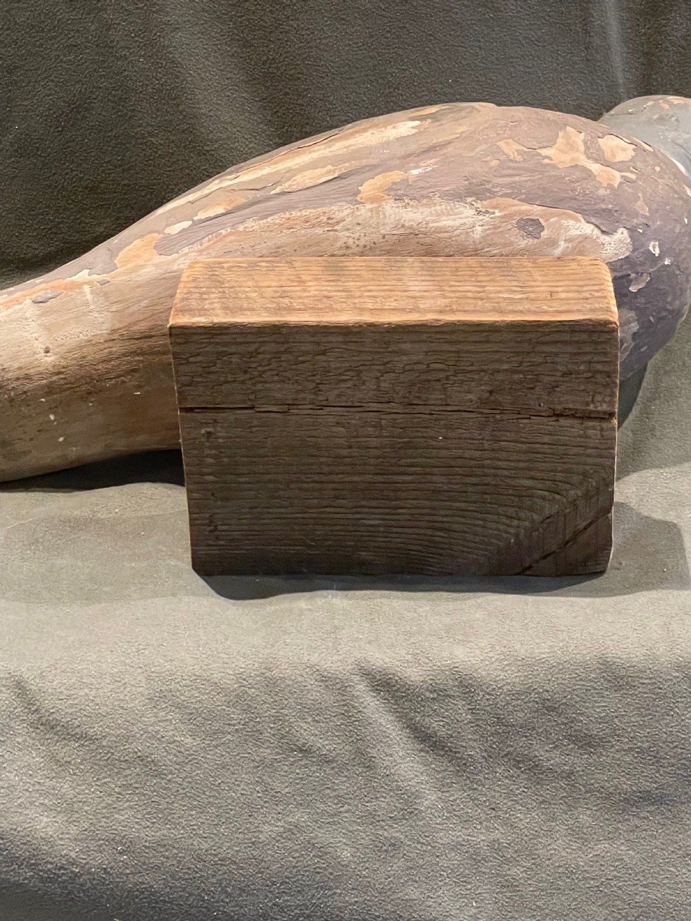 A hand-carved wooden pigeon decoy featuring weathered grey paint, mounted on a small rectangular wooden block. View XV