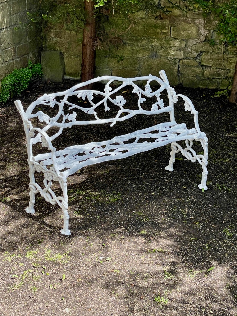 A painted white Victorian cast iron garden bench featuring an intricate intertwined branch and twig motif.
