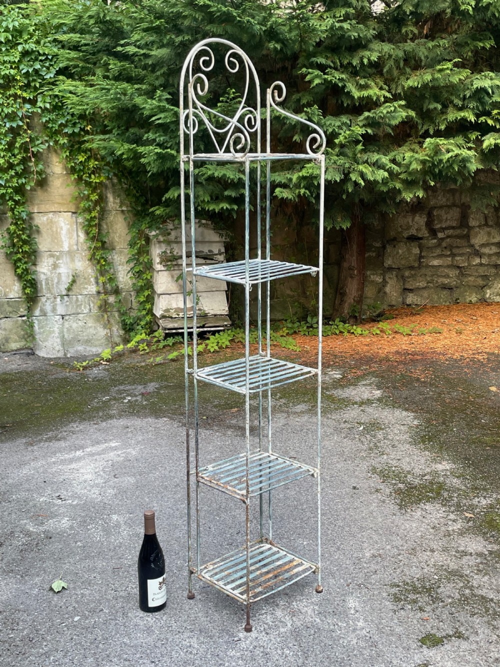 A tall, narrow painted metal plant stand with five slatted shelves and scrollwork decorative detailing at the top. View II